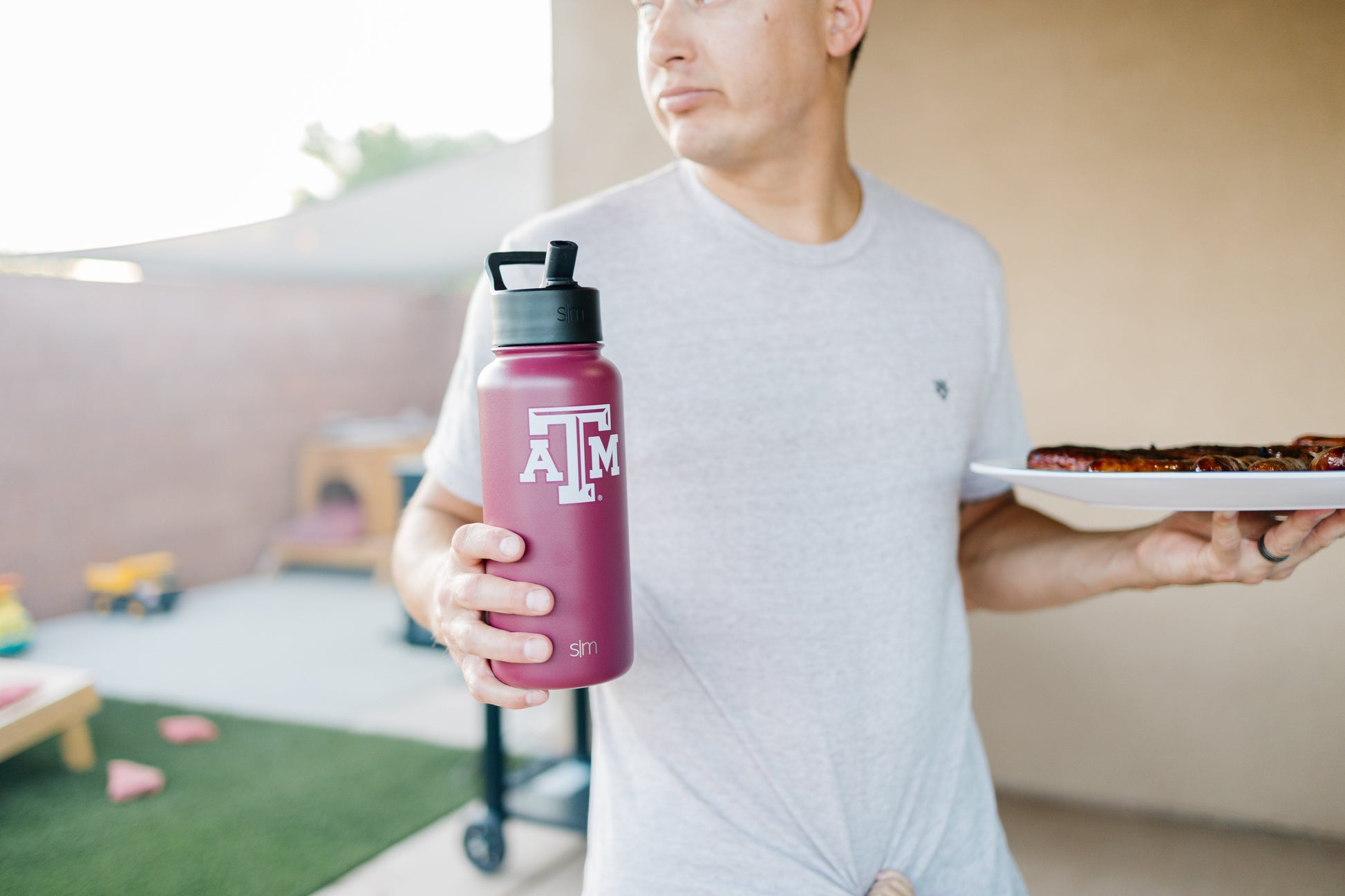 Man in light gray t-shirt holding a deep burgundy water bottle against a warm neutral background with burgundy accents